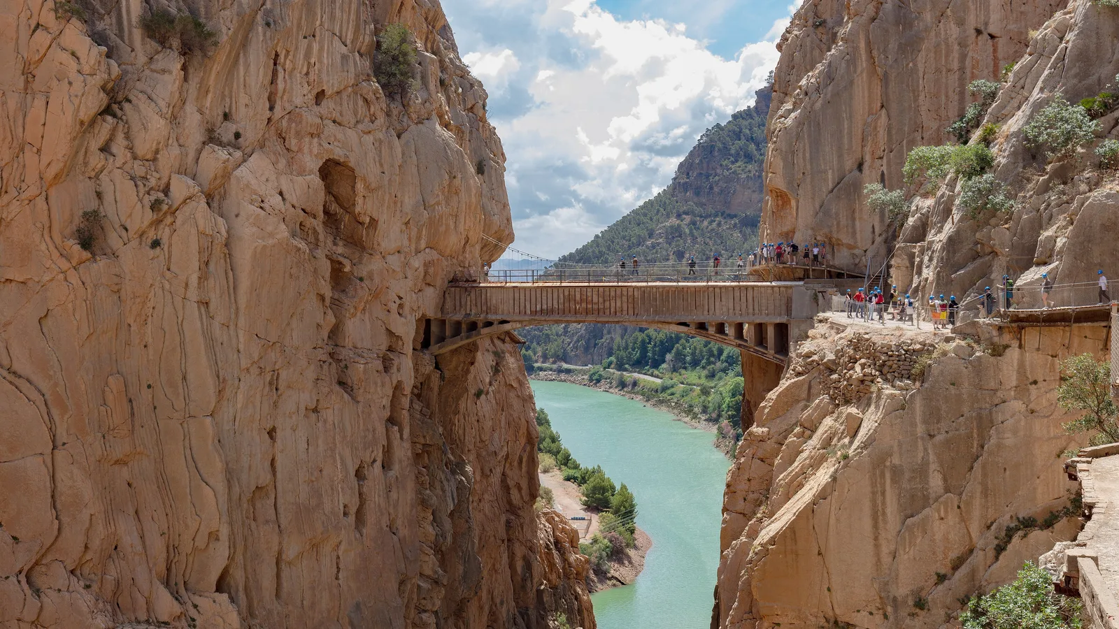 The Caminito del Rey footbridge spanning the Desfiladero de los Gaitanes, walkers strung along the boardwalk on the rock face above the turquoise river