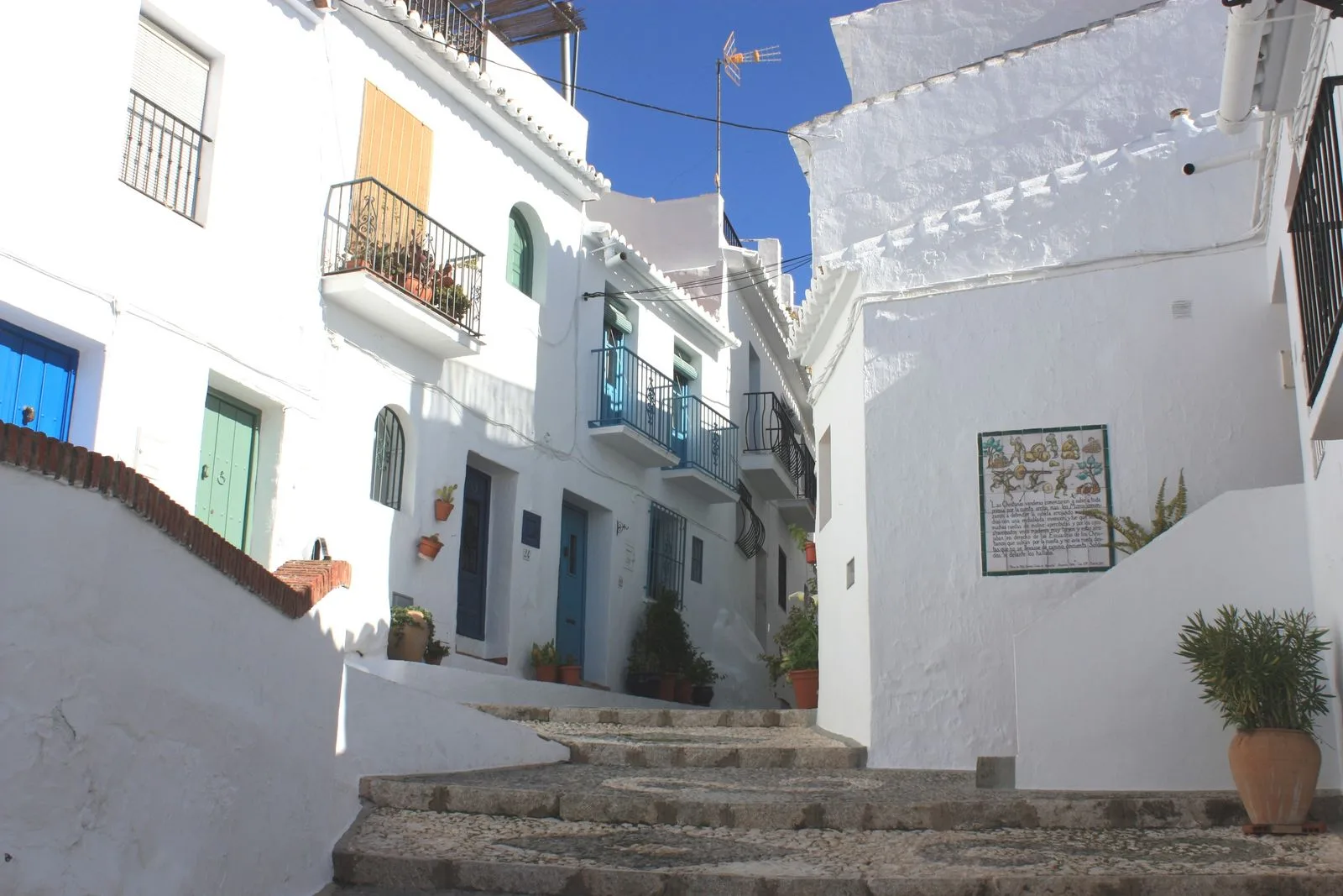 Narrow whitewashed street in Frigiliana old town with potted plants and a restaurant terrace